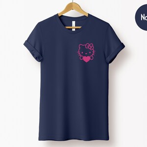 May include: Navy blue t-shirt featuring a pink Hello Kitty graphic on the chest. The graphic includes the character's face, bow, and a heart. The shirt has short sleeves and a crew neck.