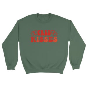 May include: A green sweatshirt featuring the text "IRISH KISSES" in red and orange. The lettering has a retro design. The sweatshirt has a crew neck and is a solid colour.