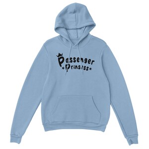 May include: A pale blue hoodie featuring a hood and a front pocket. The black text on the front reads "Passenger Princess", with a crown above "Passenger" and stars flanking "Princess".
