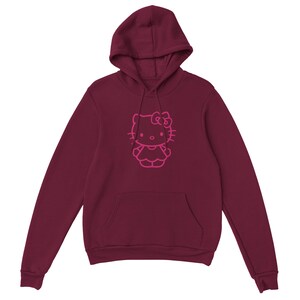May include: Burgundy hoodie featuring a pink outline of a cartoon cat character. The hooded sweatshirt has a kangaroo pocket and a drawstring. The cat character has a bow and is wearing a dress. The hoodie is made of a soft material.
