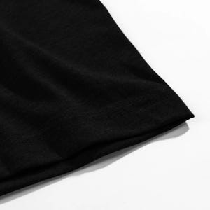 May include: Close-up of a black t-shirt, highlighting the fabric's texture and the stitched hem. The image focuses on the garment's dark colour and construction details, suitable for apparel listings.