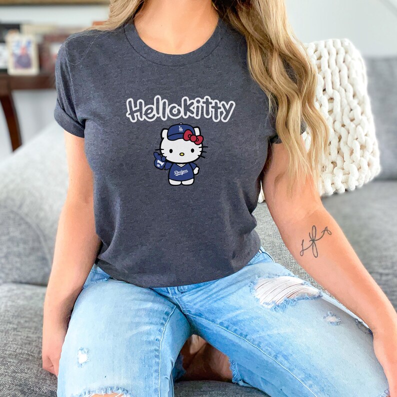 May include: Dark grey t-shirt with the text "Hellokitty" above a cartoon Hello Kitty character wearing a baseball cap and a Dodgers uniform. The character is holding a baseball glove.