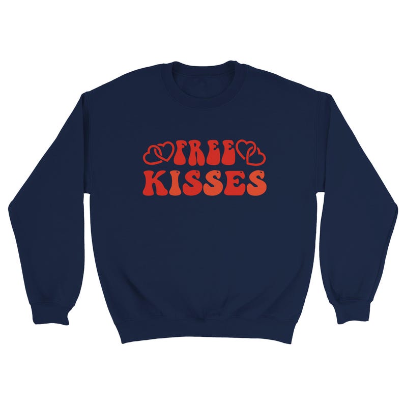 May include: Navy blue sweatshirt featuring the text "FREE KISSES" in a retro style. The lettering is in shades of orange and red, with heart motifs. A relaxed, everyday garment.