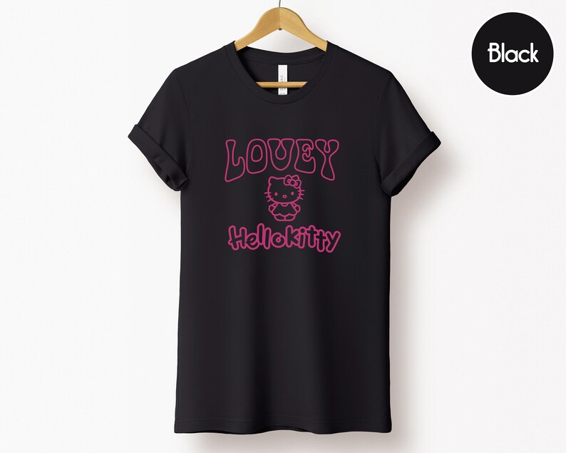 Op de afbeelding: Zwart T-shirt met de tekst "LOVEY HelloKitty" in roze, met een Hello Kitty-afbeelding. Het T-shirt wordt op een houten hanger tegen een witte achtergrond getoond. Het woord "Black" staat in een zwarte cirkel rechtsboven.