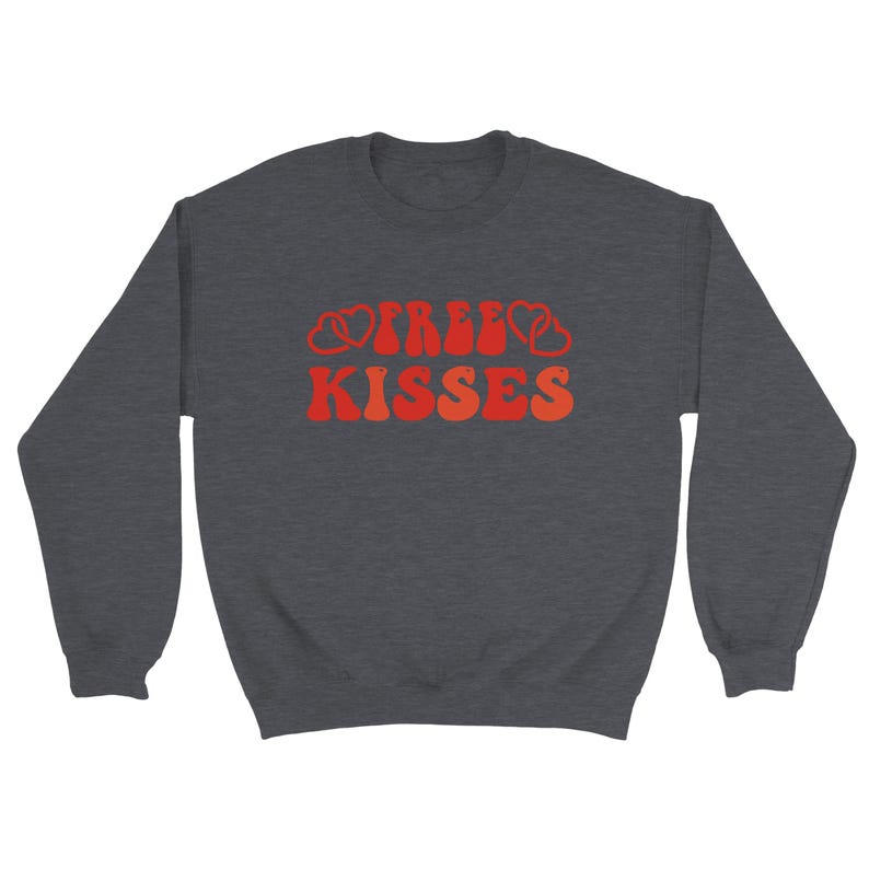 May include: A dark grey sweatshirt featuring the text "FREE KISSES" in a retro font. The words are in shades of orange and red, with heart shapes integrated into the design. A casual, comfortable top.