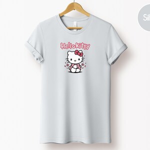May include: A light gray t-shirt featuring a Hello Kitty graphic. The graphic includes the text "Hello Kitty" in pink above an illustration of the character with a pink bow and flowers.