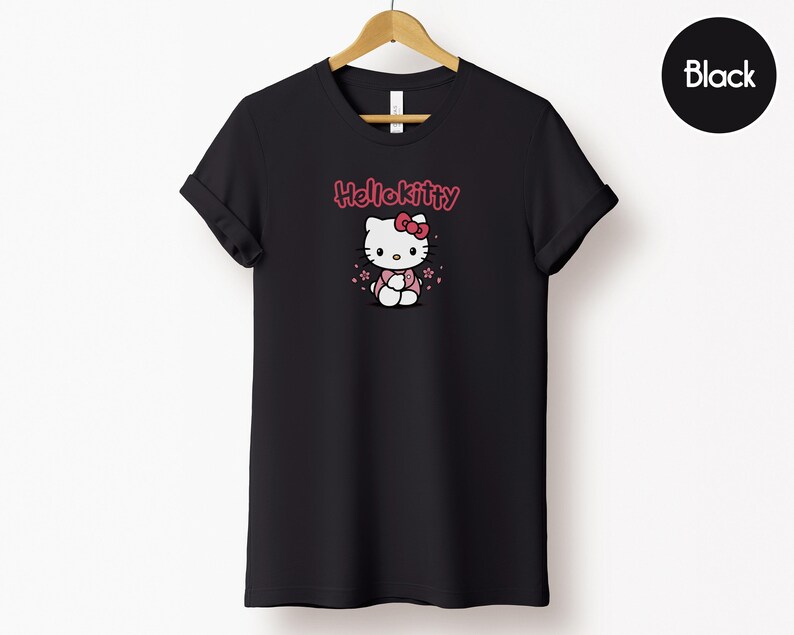 May include: Black t-shirt featuring a Hello Kitty graphic. The design includes the text "Hello Kitty" in pink above an illustration of the character. The shirt is displayed on a wooden hanger against a white background.