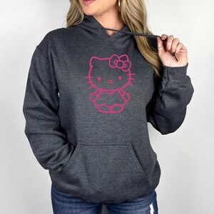 May include: Dark gray hooded sweatshirt featuring a pink outline of a cartoon cat character. The sweatshirt has a front pocket and a drawstring hood. The graphic is centered on the chest.