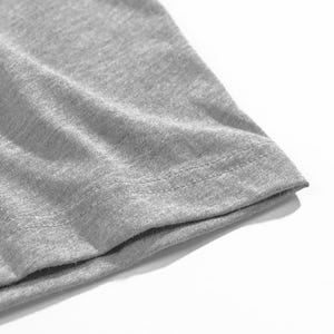 Op de afbeelding: Close-up van een grijze t-shirtmouw. De stof is een zacht, gem&ecirc;leerd grijs, met zichtbare textuur. De zoom is netjes gestikt met een dubbele rij draad.