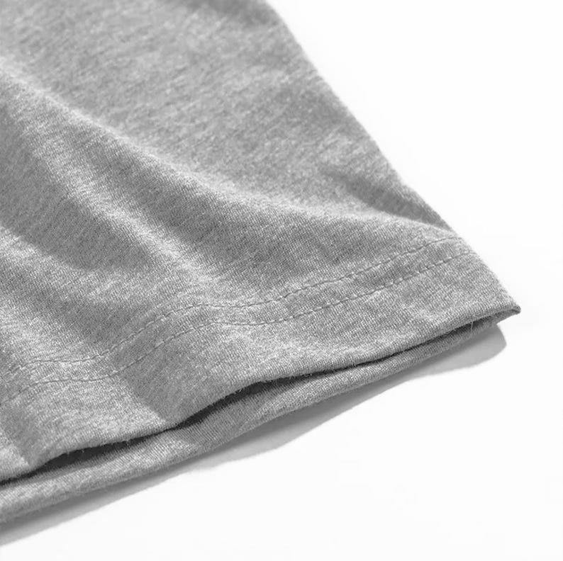 Op de afbeelding: Close-up van een grijze t-shirtmouw. De stof is een zacht, gem&ecirc;leerd grijs, met zichtbare textuur. De zoom is netjes gestikt met een dubbele rij draad.