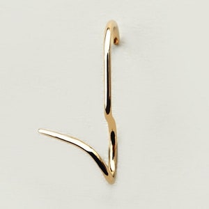 May include: A gold-colored, abstract earring with a curved design. The earring has a long, vertical element that curves at the top and a shorter, horizontal element at the bottom. The earring is set against a plain, off-white background.