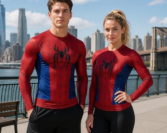 May include: A long-sleeved compression shirt featuring a red and blue spiderweb pattern with a black spider emblem on the chest. The garment has a crew neckline and is designed with a fitted silhouette, showcasing the iconic superhero-inspired aesthetic.