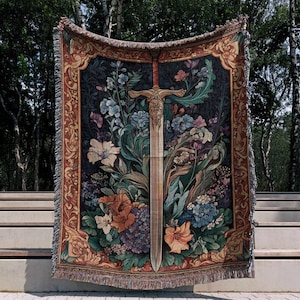 Puede incluir: Una manta de tapiz decorativa con un dise&ntilde;o de espada en medio de un arreglo floral. La manta tiene un fondo oscuro con flores coloridas en tonos de azul, naranja y morado. El borde es marr&oacute;n c&aacute;lido con patrones decorativos.