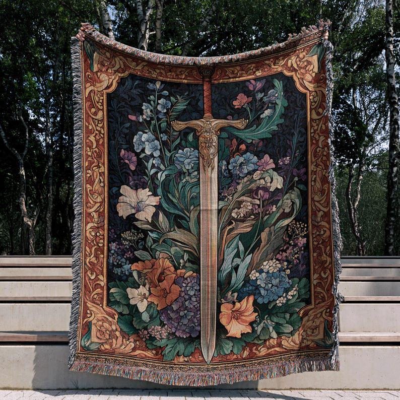 Puede incluir: Una manta de tapiz decorativa con un dise&ntilde;o de espada en medio de un arreglo floral. La manta tiene un fondo oscuro con flores coloridas en tonos de azul, naranja y morado. El borde es marr&oacute;n c&aacute;lido con patrones decorativos.