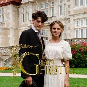 Puede incluir: Un hombre con traje negro y una mujer con vestido blanco frente a un gran edificio de piedra. La imagen tiene el texto "GRAN HOTEL" en oro. La escena se desarrolla en un césped verde con flores rojas.