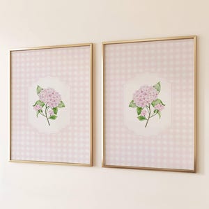 Op de afbeelding: Twee ingelijste kunstdrukken met aquarel hortensia bloemen. Het kunstwerk heeft een roze en witte ruitjes achtergrond, met een gouden lijst. De hortensia is zachtroze met groene bladeren.