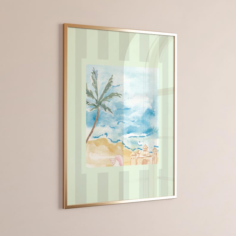 Puede incluir: Impresi&oacute;n enmarcada de acuarela de una escena de playa con una palmera, arena y un castillo de arena. La obra de arte est&aacute; enmarcada en un marco de metal dorado y sobre un fondo a rayas verde claro.