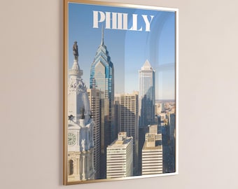 May include: Framed print featuring a cityscape of Philadelphia, Pennsylvania, under a clear blue sky. The word "PHILLY" is displayed in white at the top. The image showcases iconic buildings, including a skyscraper with a blue glass facade.