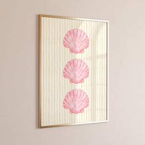 May include: A framed art print featuring three pink seashell illustrations. The seashells are arranged vertically against a background of yellow and white vertical stripes. The frame is gold-colored.