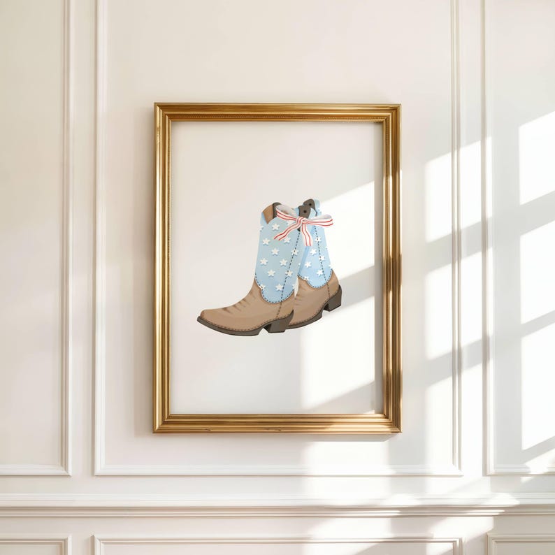 May include: A framed print of a cowboy boot. The boot is tan with a light blue shaft adorned with white stars. A red, white, and blue bow decorates the top. The frame is gold, set against a white wall.