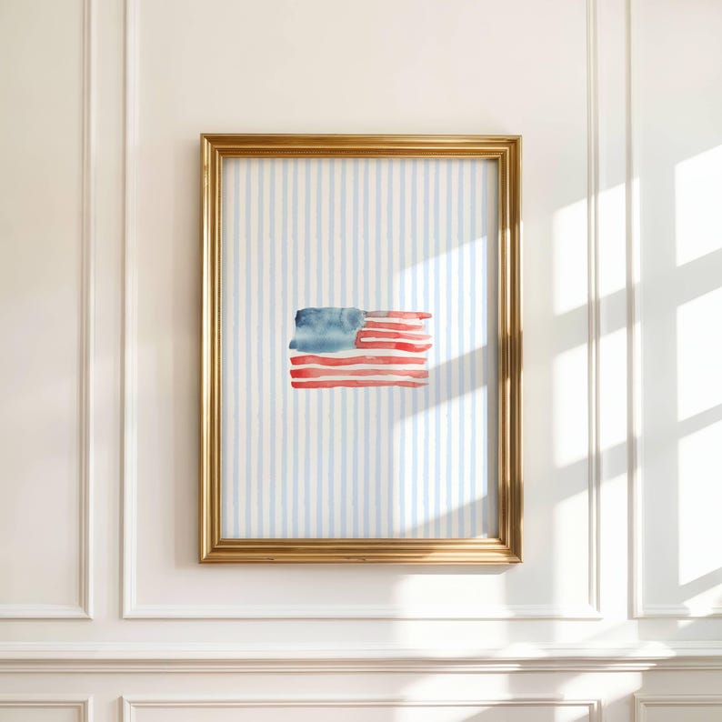 May include: A framed watercolor painting of the American flag. The flag is depicted with red and blue brushstrokes, set against a light blue and white striped background. The frame is gold.