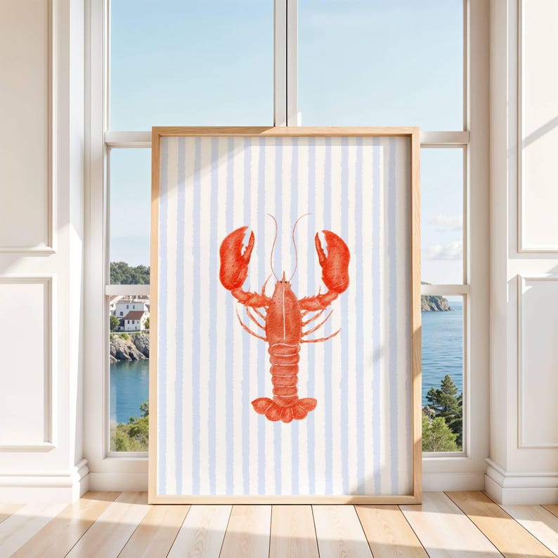 Op de afbeelding: Een ingelijste kunstdruk met een illustratie van een rode kreeft. De kreeft staat tegen een achtergrond van verticale blauwe en witte strepen. Het kunstwerk wordt gepresenteerd in een licht houten frame, ideaal voor kust- of nautische decoratie. Afmetingen: 50 x 70 cm.