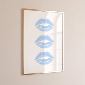 Könnte beinhalten: Gerahmter Kunstdruck mit drei blauen Lippenabdrücken auf weißem Hintergrund. Das Kunstwerk befindet sich in einem goldfarbenen Rahmen mit Glasabdeckung. Die Lippenabdrücke sind vertikal angeordnet und haben eine strukturierte Optik. Modernes und stilvolles Design.
