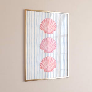 May include: A framed art print featuring three pink seashell illustrations on a background of blue and white vertical stripes. The artwork is encased in a gold-coloured frame, creating a coastal theme.