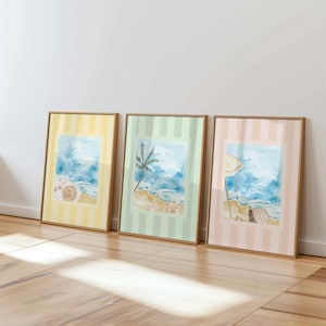 Puede incluir: Tres impresiones enmarcadas de escenas de playa. Cada impresi&oacute;n presenta una pintura de acuarela de una playa con cielos azules y oc&eacute;ano. Los marcos tienen un fondo a rayas en amarillo, verde y rosa. Los marcos son de madera.