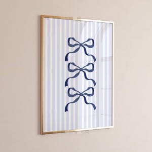 Puede incluir: Arte de pared enmarcado con un fondo a rayas azules y blancas y tres ilustraciones de lazos azul marino. La obra de arte se presenta en un marco dorado. Los lazos están espaciados uniformemente, creando un diseño equilibrado y decorativo.