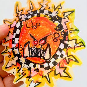 Peut inclure: Un autocollant dessiné à la main représentant un visage de dessin animé en colère avec des dents pointues et des yeux rouges. Le visage est orange, entouré d'un motif à carreaux noir et blanc et d'éclairs jaunes. Le bord de l'autocollant est irrégulier.