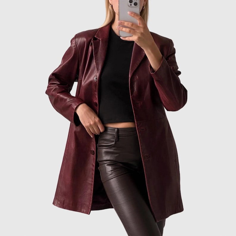 May include: A burgundy leather blazer with a classic lapel collar and button closure. The longline coat is paired with a black top and burgundy leather pants. The blazer has a tailored fit and a polished appearance.
