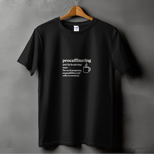 Puede incluir: Camiseta negra con la palabra "procaffinating" y su definición impresa en blanco. La definición incluye la pronunciación, la parte de la oración y un pequeño gráfico de taza de café.