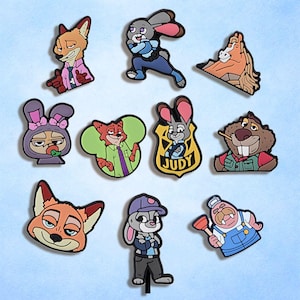 May include: A collection of colorful cartoon character charms, featuring a fox in a pink shirt, a rabbit in a police badge with the name "Judy", and other animal characters. The charms are likely for shoes or accessories.