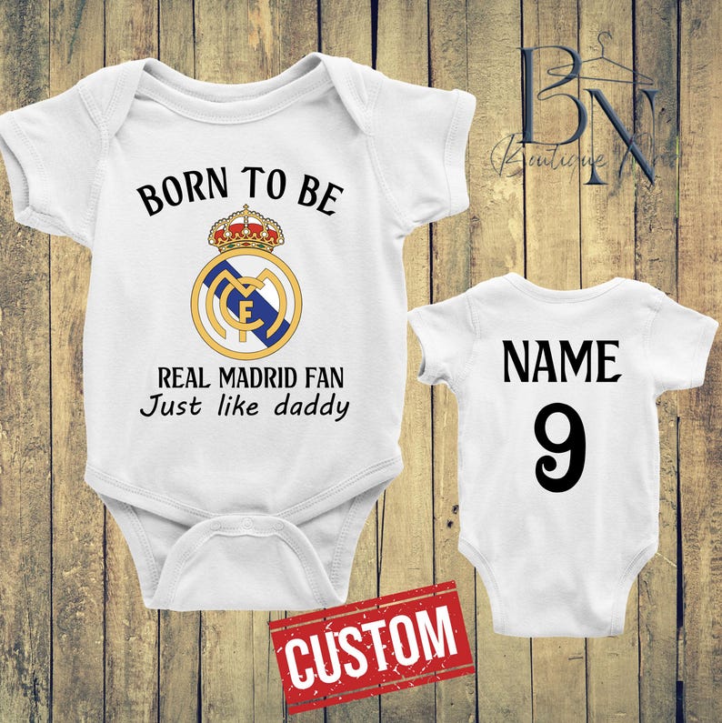 May include: Two white baby onesies. One has the Real Madrid logo and the text "BORN TO BE REAL MADRID FAN Just like daddy". The other has "NAME" and the number "9". A red "CUSTOM" stamp is at the bottom.