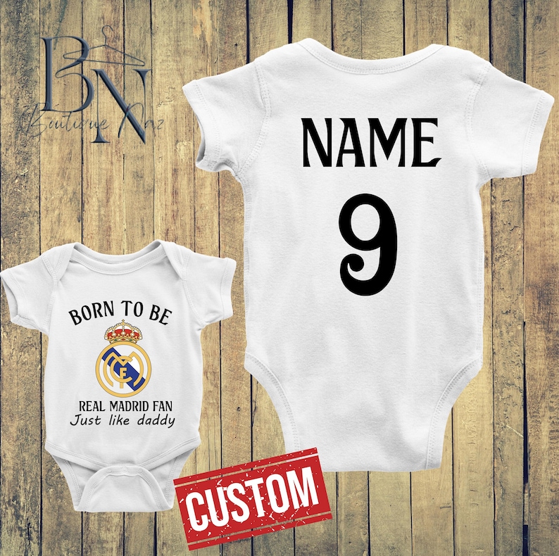 May include: Two white baby onesies. One has the text "BORN TO BE REAL MADRID FAN Just like daddy" with a team logo. The other has the text "NAME" and the number "9". A red "CUSTOM" stamp is visible.