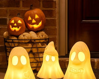 May include: Halloween decorations featuring illuminated ghost figures and carved pumpkins. A sign reads "Trick or Treat" above the pumpkins. The ghosts have glowing eyes and some have heart or "BOO" details. The pumpkins and ghosts are lit with a warm, inviting glow.