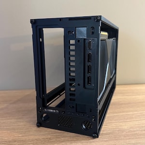 May include: A black computer case with an open frame design. The case features multiple ports and openings for components, including a graphics card. The case is designed to house computer hardware and components.