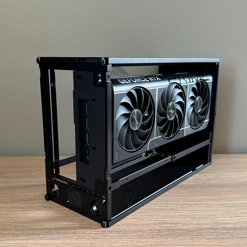 May include: A black computer case with a GeForce RTX graphics card. The graphics card has three fans and the text "GEFORCE RTX" is visible. The case is rectangular and has a minimalist design.