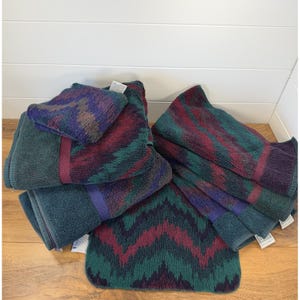 May include: A set of plush bath towels and a matching bath mat featuring a repeating chevron pattern in deep shades of teal, burgundy, and purple. The towels have a thick, absorbent texture with solid teal borders and visible white care tags.