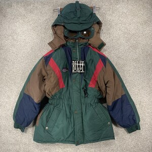 May include: A vintage winter jacket with a green, brown, navy, and red color scheme. The jacket features a hood with attached goggles and the text "BILLY" on a tag. The jacket has a drawstring waist and multiple pockets.