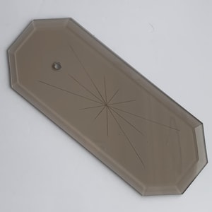 May include: A rectangular, light brown glass lampshade with a starburst design etched into the surface. The lampshade has a small hole near one end for mounting. The edges are beveled, and the overall shape is elongated.