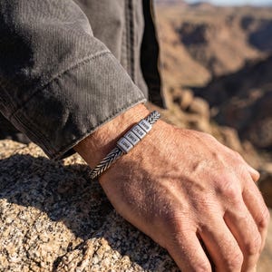 Puede incluir: Una pulsera de metal trenzado en tono plateado con cuatro cuentas rectangulares grabadas con los nombres David, Chloe, Emily y Luna. La pulsera tiene una apariencia tejida y texturizada, y se lleva alrededor de la muñeca con un acabado metálico.