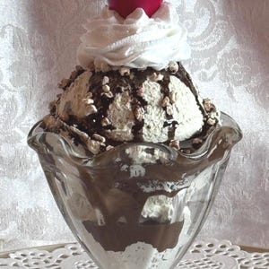 May include: A white ceramic mug with a black handle and the text "But First, Coffee" in a handwritten style. The mug is on a white surface. The mug is approximately 4 inches tall.