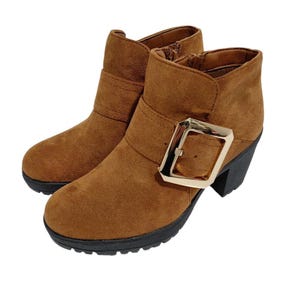 May include: A pair of brown suede ankle boots with a gold-colored buckle and a black heel. The boots have a round toe and a side zipper. The heel height is approximately 3 inches.