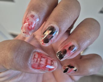 May include: A hand with clear acrylic nails featuring a red and black design. One nail has the word "HELP" written in red. The other nails have a splatter and geometric design.