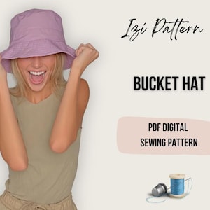 May include: A light purple bucket hat is held up by a person. The image includes the text "Bucket Hat" and "PDF Digital Sewing Pattern". A spool of blue thread and a thimble are also visible.