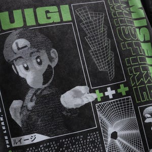 May include: Dark gray t-shirt featuring a graphic of Luigi from the Super Mario Bros. series. The design includes the word "Luigi" in green, along with other text and geometric shapes. The shirt has a vintage, distressed look.