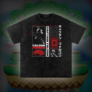 Może przedstawiać: Ciemnoszara koszulka z nadrukiem graficznym. Projekt zawiera słowa "CAPTAIN FALCON" i "FALCON PUNCH" w kolorze czerwonym i białym, a także obrazy postaci w akcji i japoński tekst.