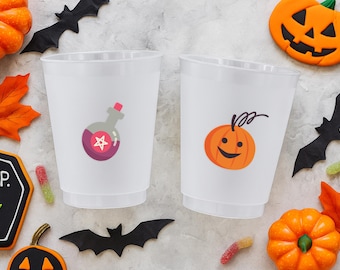 May include: Two white plastic cups with Halloween-themed designs. One cup features a potion bottle with a star, and the other has a smiling jack-o'-lantern. The cups are surrounded by Halloween decorations, including pumpkins, bats, and leaves.